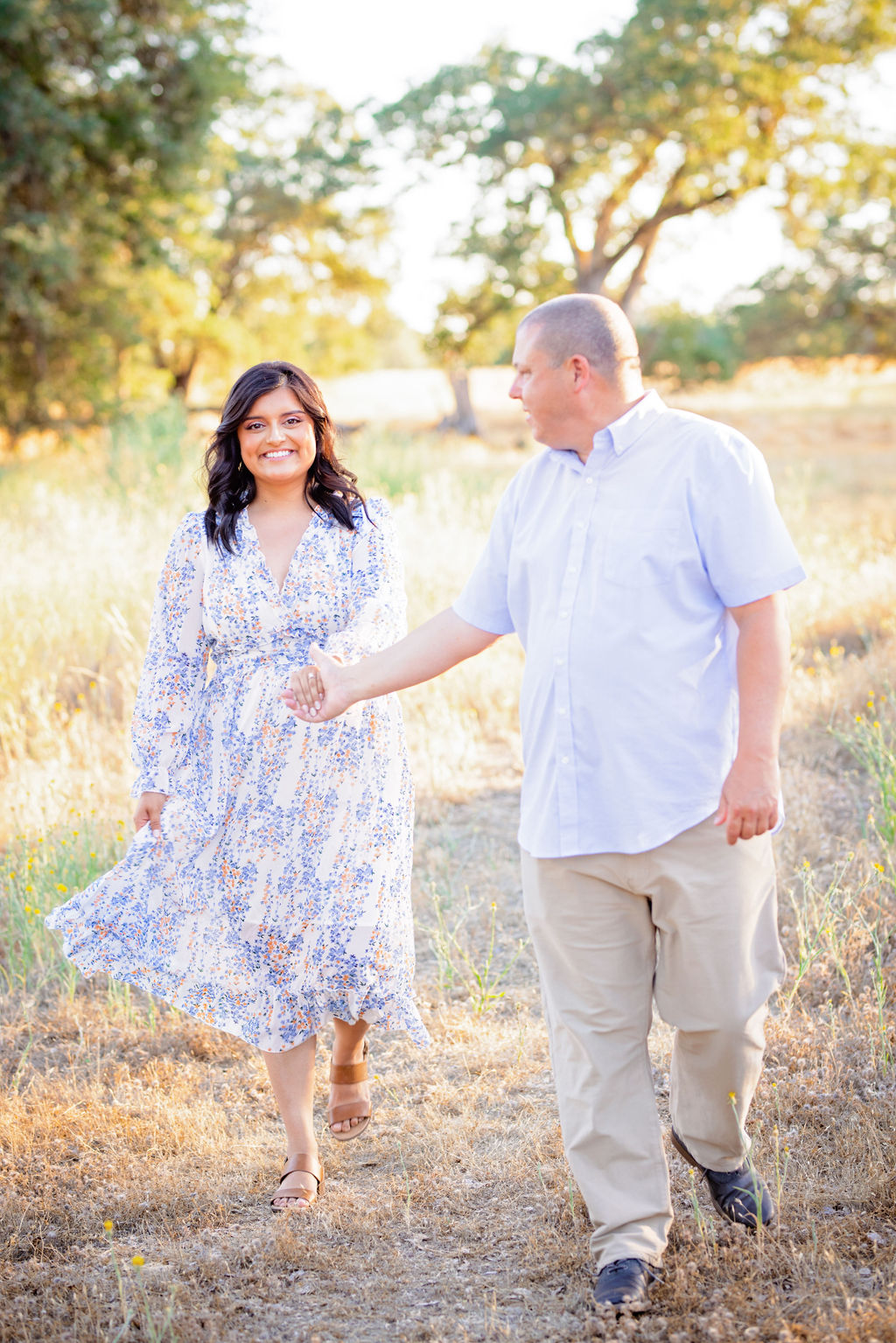 bride and groom to be in neutral colors laughing in a sunny field