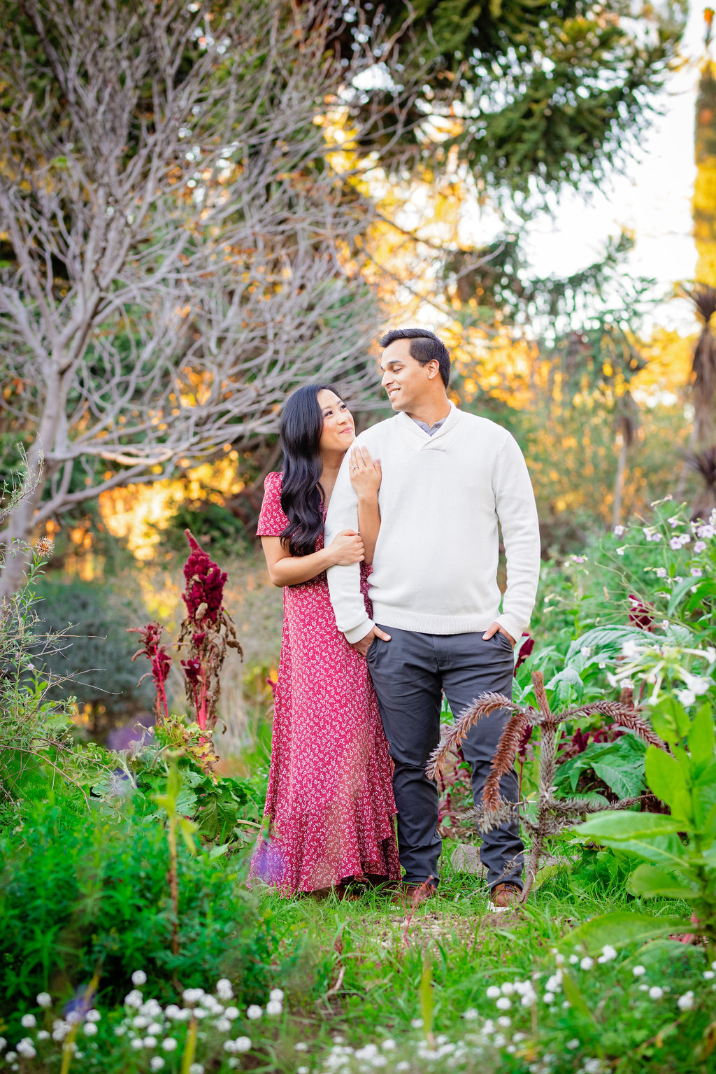Woman holding on to man in a garden at sunset in William Land Park Sacramento Engagement Photo Locations