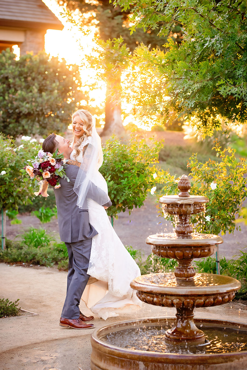 groom lifting his bride and laughing near a fountain at their Wolfe Heights Wedding