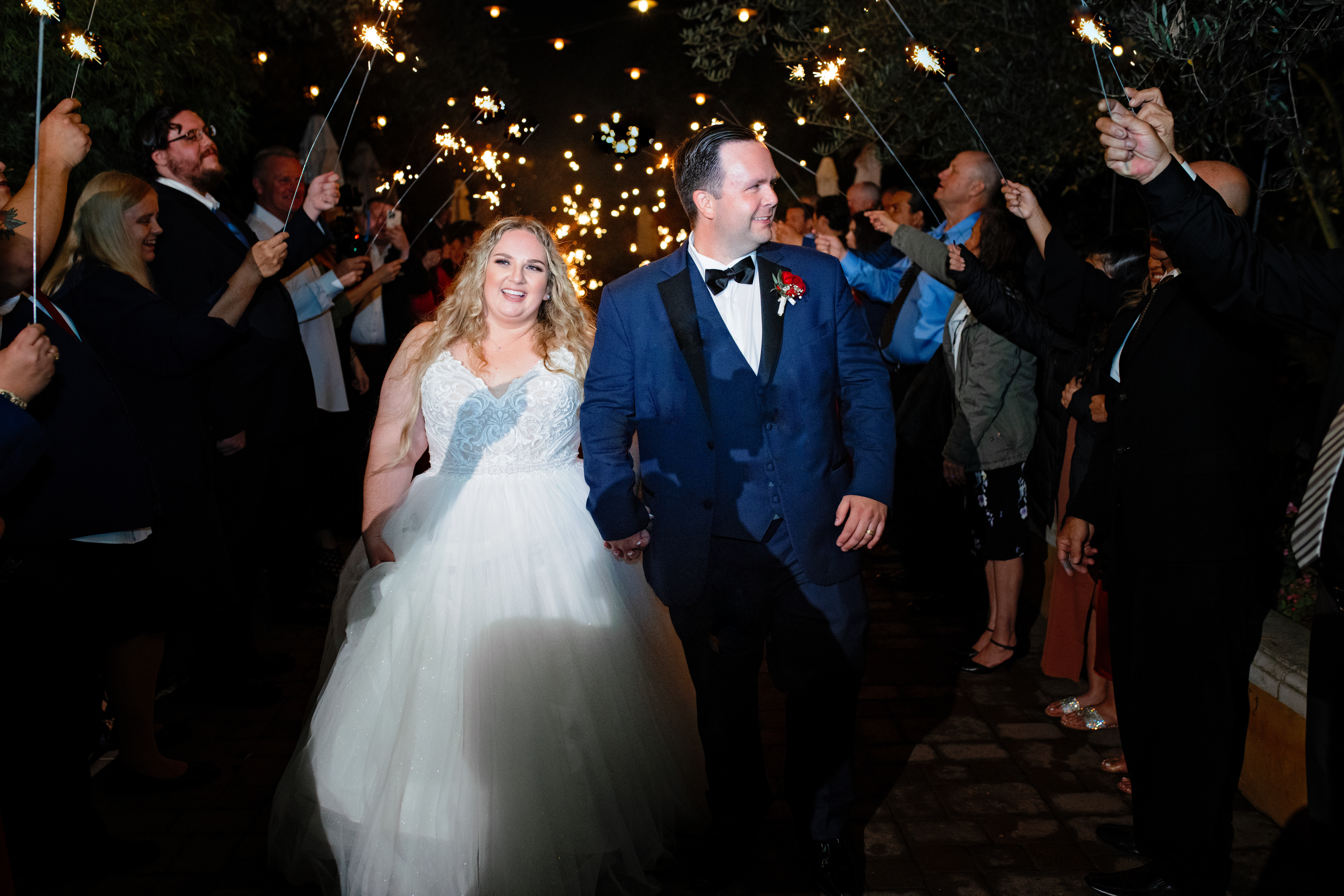 Newlyweds walking happily out of their Viaggio Winery wedding while guests hold up lit sparklers