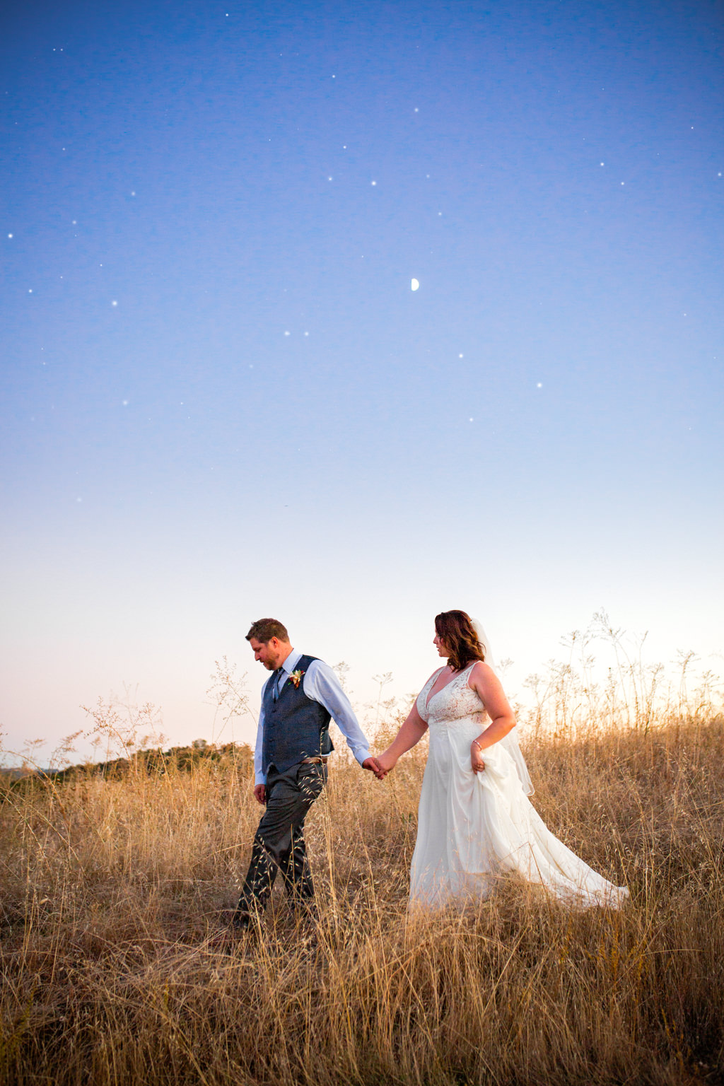 Night time shot of bride and groom holding hands and walking down hill at rancho victoria weddings with the moon and stars in the background